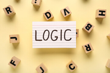 Paper with word LOGIC and wooden cubes on yellow background