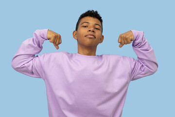 Young brown skinned Latino man making a gesture of strength with his hands, he is wearing a lilac sweatshirt on a light blue background, concept of youthful strength