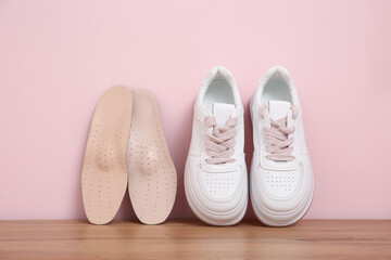 Sneakers with orthopedic insoles on bench near pink wall