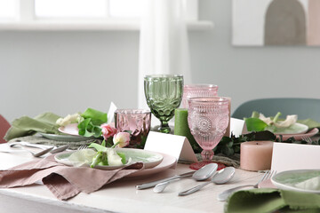 Elegant table setting with beautiful flowers and green leaves in light dining room, closeup