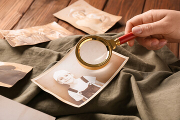 Female hand with magnifier and old photos of relatives. Concept of family tree