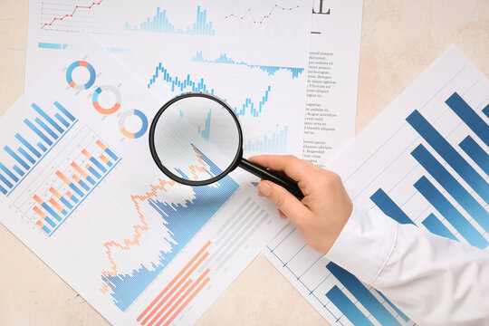 Female hand with magnifier and business charts on white background