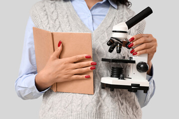 Female teacher with microscope and book on light background, closeup