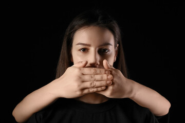 Hands covering mouth of young woman on black background. Concept of oppression