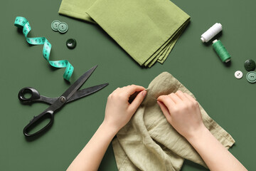 Female hands sewing clothes on green background