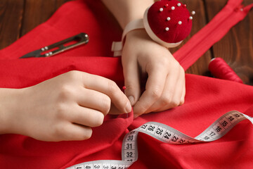 Female hands sewing red clothes on wooden background, closeup