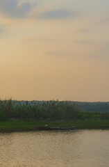 Abandoned boat on the edge of the lake in the afternoon with red sky and green grass