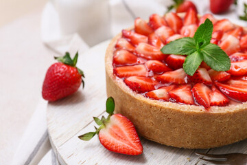 Wooden board of sweet strawberry tart with mint on white background, closeup