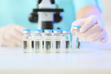 Female scientist with ampules and microscope at table in laboratory, closeup