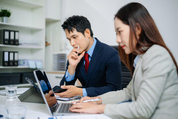 Young Asian businessman and colleague using laptop and tablet while discussing project in modern office. Consulting, teamwork, strategy