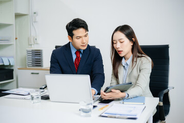 Young Asian businessman and colleague using laptop and tablet while discussing project in modern...