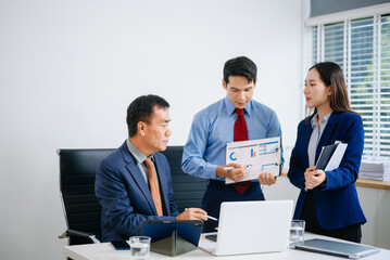 Asian executives discussing financial data and charts in a modern office setting. Teamwork, decision making, leadership
