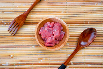 raw minced beef in a wooden bowl lined with rattan weaving with a spoon and fork beside it