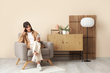 Young woman using mobile phone in grey armchair at home