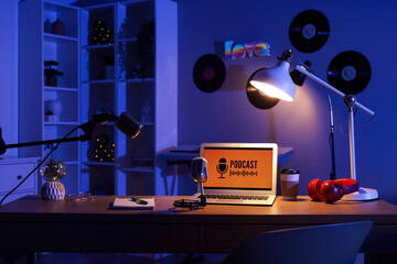 Podcaster's workplace with laptop, microphones and glowing lamp in dark studio
