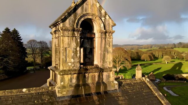 stone-faced - Aerial view of a historic bell tower with a visible bell, surrounded by lush green fields and trees, under a partly cloudy sky, capturing the serene landscape