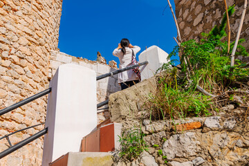 A woman takes a close up photo of a Barbary macaque as it sits on a wall at the medieval Moorish...