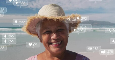 Senior woman smiling at shoreline while social media icons rising showing engagement then fading - Powered by Adobe