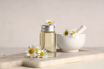 Bottle of chamomile cosmetic oil and mortar with flowers on white background