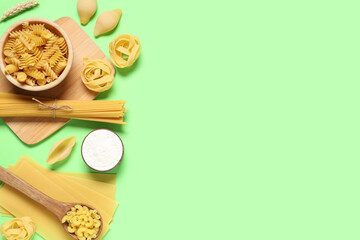 Composition with different types of raw tasty pasta, wooden bowl, spoon and cutting board on green...
