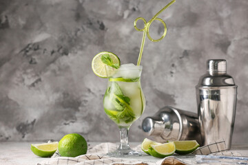 Glass of tasty mojito, napkin and lime on grey grunge background, closeup
