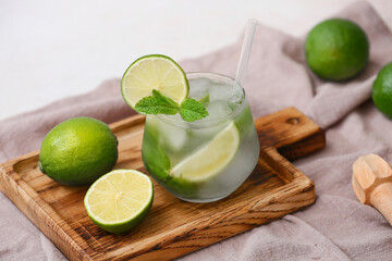 Composition with wooden cutting board, glass of tasty mojito, napkin and ingredients on white...