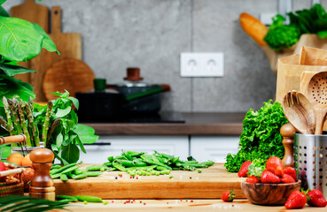 Fresh vegetables, green peas and herbs arranged on a wooden cutting board in a modern kitchen for healthy cooking