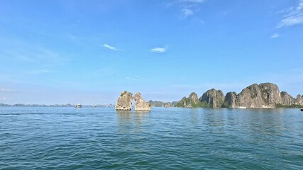Limestone islets known as the Kissing Rocks, rising from the calm emerald waters of Ha Long Bay, Vietnam, under a clear blue sky.