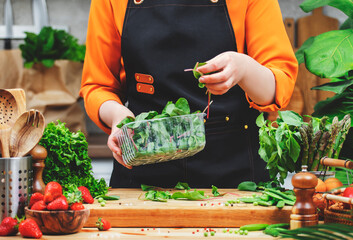 Chef woman in apron carefully arranges fresh shard while surrounded by various vegetables and fruits in a warm kitchen setup