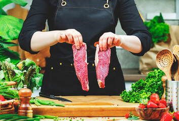 Chef cooking food in the kitchen. Cook hands holds separate fresh beef steak amidst vegetables on wooden cutting board