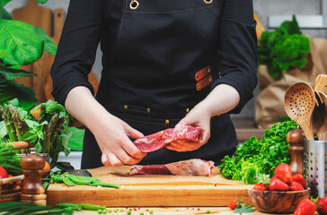 In a cozy kitchen, a woman chef holds raw beef steak skillfully prepares fresh ingredients, showcasing her passion for healthy, vibrant cooking.