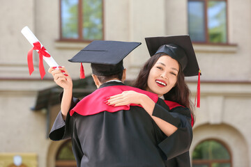 Couple of happy graduating students with diploma hugging near university