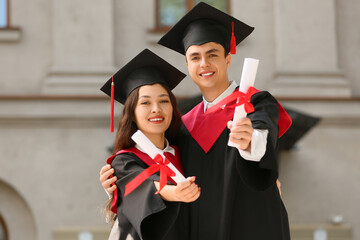 Couple of happy graduating students with diplomas hugging near university