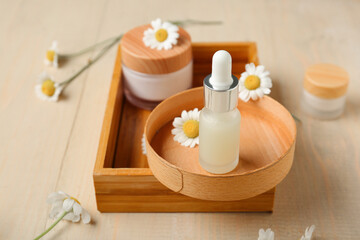 Composition with tray, chamomile flowers, bottle and jar of cosmetic products on beige wooden background, closeup