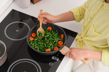Woman with spoon frying vegetables on stove in kitchen, closeup