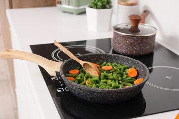 Frying pan with tasty vegetables and spoon on electric stove in kitchen, closeup