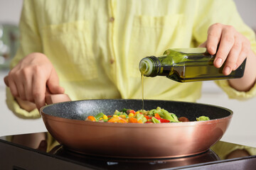 Woman with olive oil frying vegetables on mini stove in kitchen, closeup