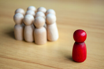 Red Wooden Figure Standing Apart From Beige Peg Group On Table