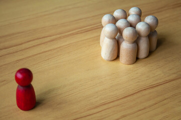 Red Figure Facing Beige Pegs In Formation On Wood Surface