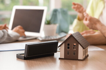 House model and pen case on table against real estate agent working with couple in office, closeup