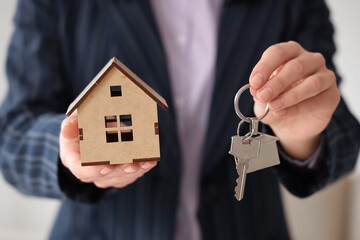 Female real estate agent with key and house figure in room, closeup