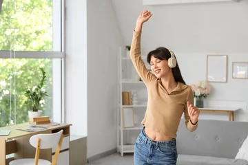 Gordijnen Smiling young woman in headphones dancing at home © Pixel-Shot
