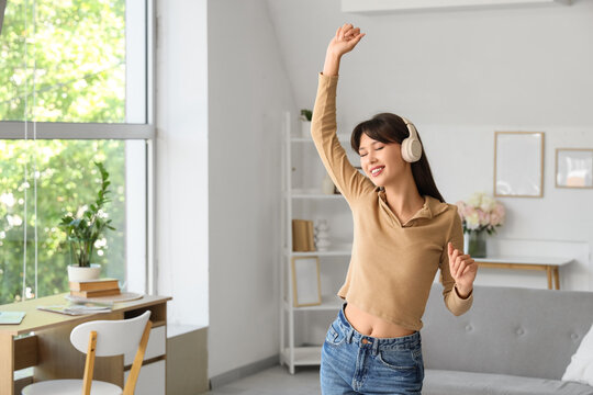 Smiling young woman in headphones dancing at home