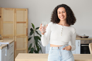Young African-American woman with glass of water in kitchen