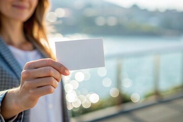 Hands holding a blank white business card against a blurred blue water background.
