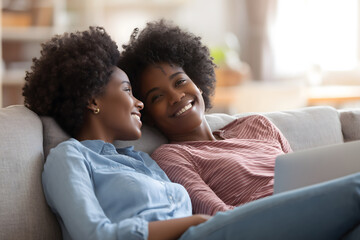 Two women relaxing on couch, sharing smiles and laughter, enjoying cozy moment together