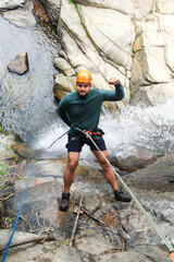 Adventurous canyoneer rappelling down a rocky waterfall, demonstrating strength and skill in...