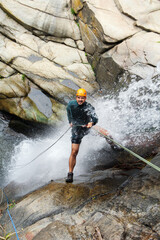 Obraz premium Latin american canyoneer rappelling down a waterfall, enjoying extreme sports and adventure in nature
