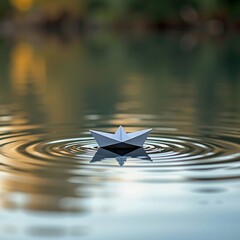 A small paper boat floats gently on calm water, creating ripples with soft light reflections and a peaceful, blurred background.