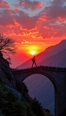 A lone hiker crosses a stone bridge at sunset with vibrant red and orange clouds over mountainous terrain.